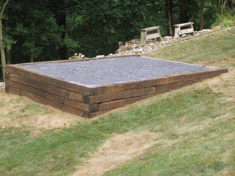 Shed pad with railroad tie wood retaining wall, built on a hillside.